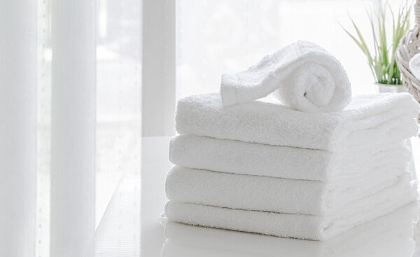 Clean white towels on white table in white room, copy space.